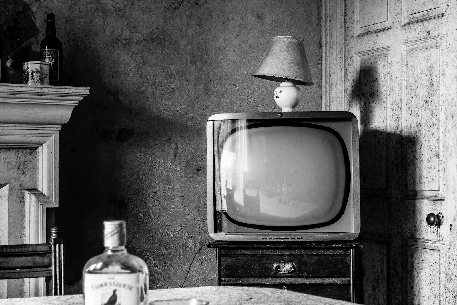 bottle of liquor on table with CRT television across beside the close door