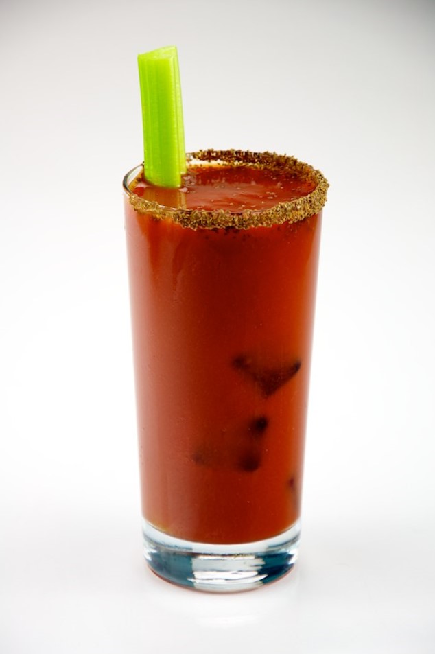 A Bloody Mary in a tall glass with a seasoned rim and a celery stalk