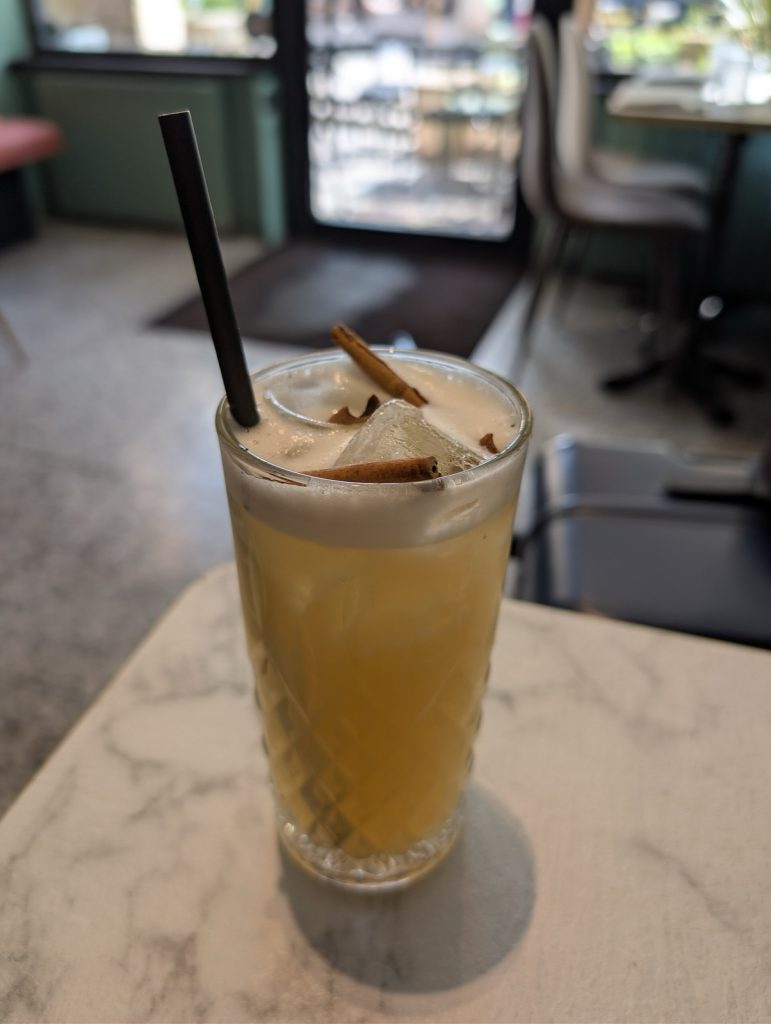 A foam-topped zero-proof cocktail garnished with cinnamon sticks